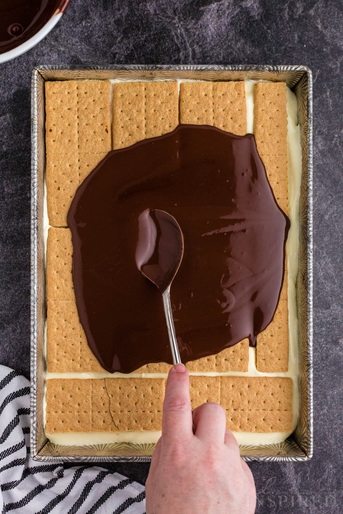 Chocolate ganache spread over the final layer of Graham crackers in a casserole dish.