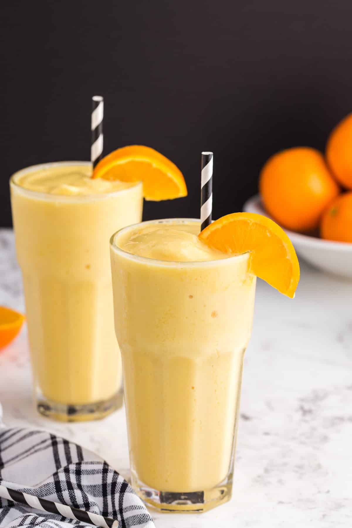 Two glasses of Orange Julius recipe with orange wedge garnish and decorative straws.