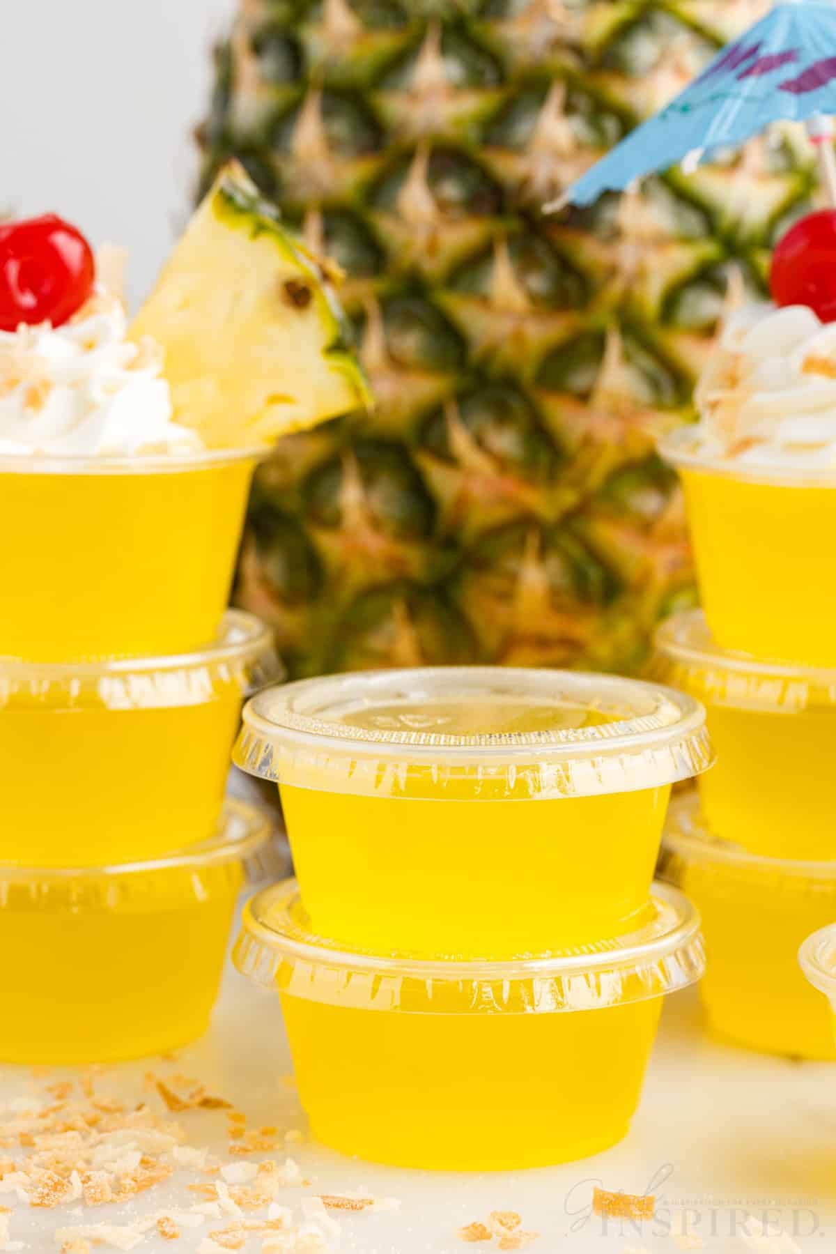Piña Colada Jello Shots stacked on each other with a pineapple in the background.