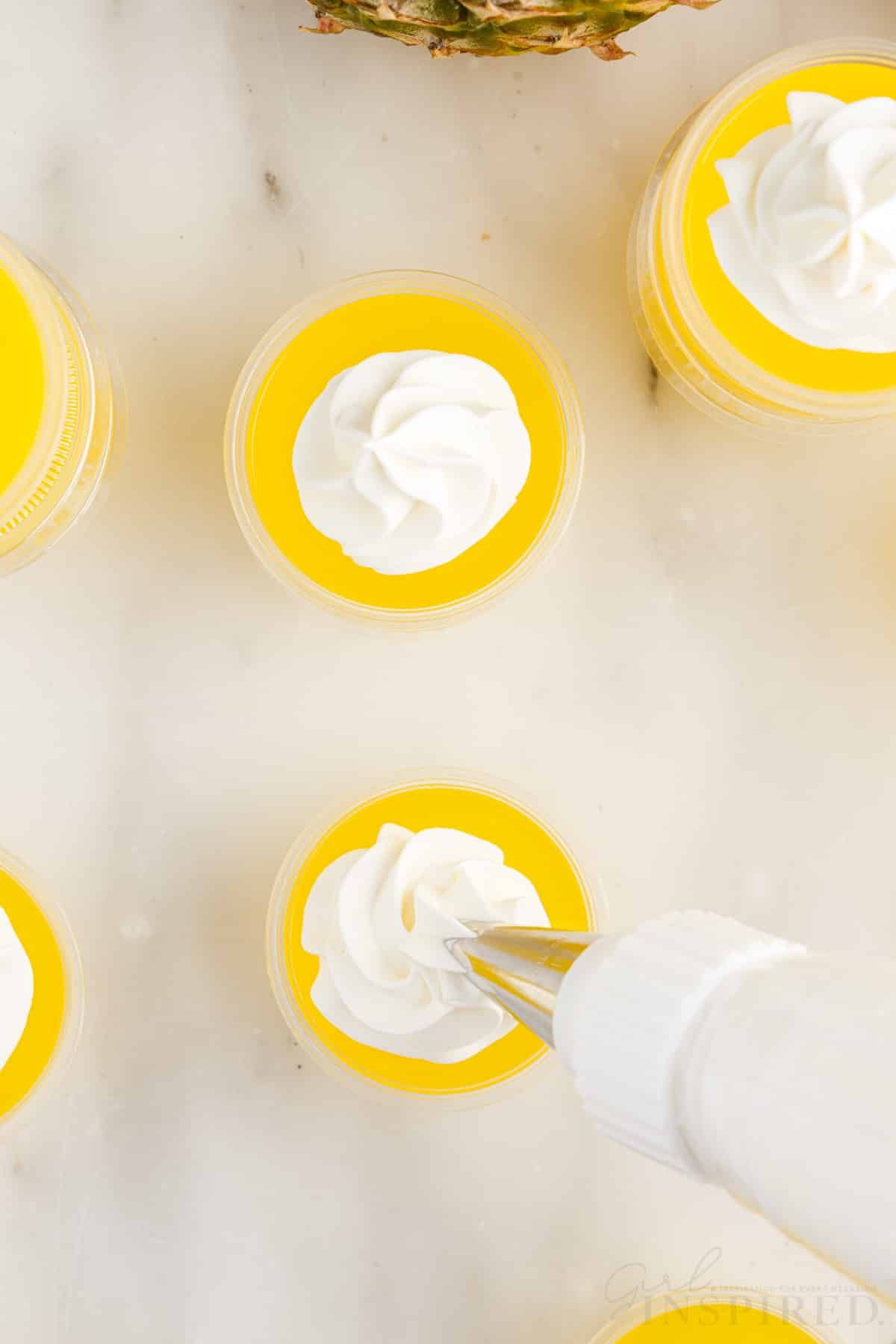 Overhead view of Piña Colada Jello Shots being topped with whipped topping.