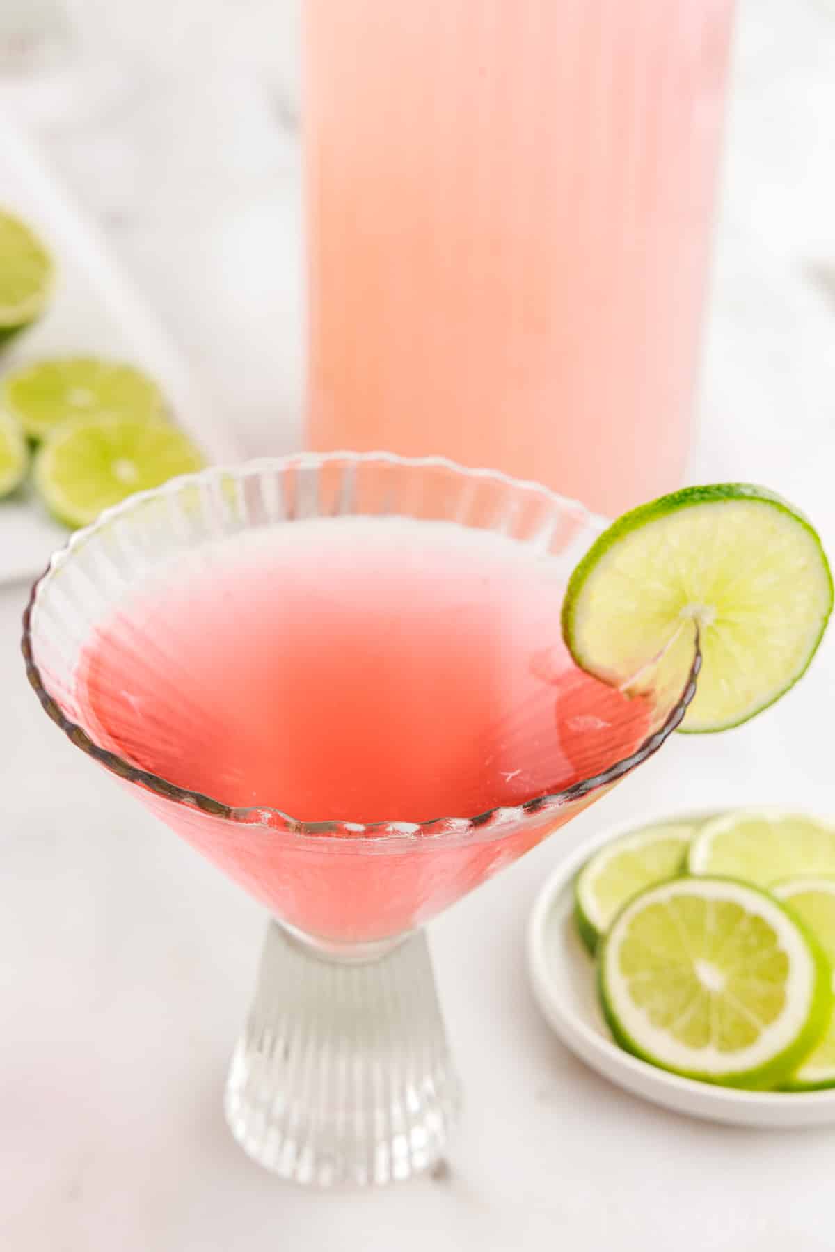 Decorative glass with Pink Flamingo Drink garnished with a lime next to a dish of limes.