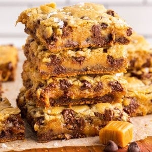 Stacked salted caramel chocolate chip cookie bars on a wooden kitchen board.