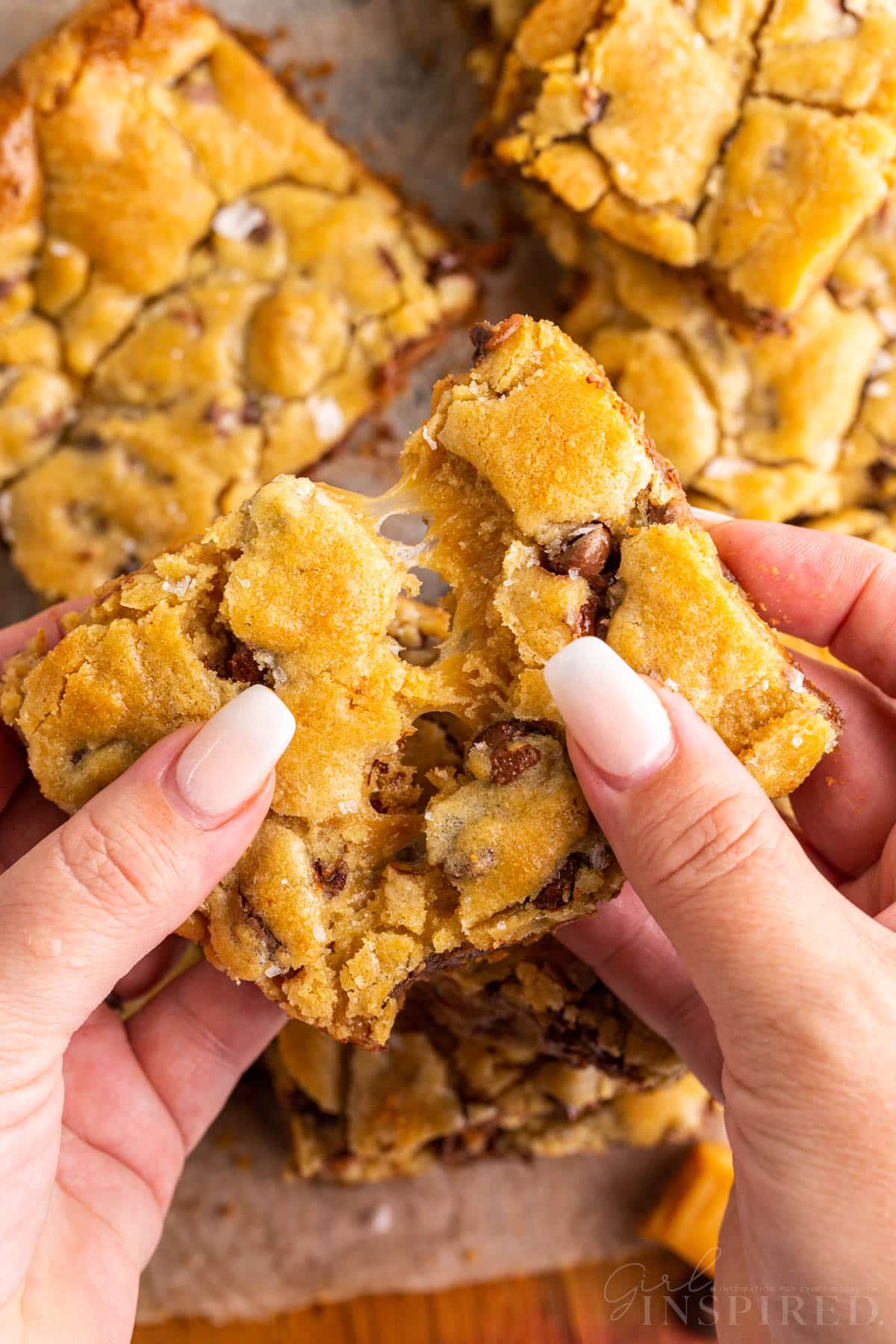 Hands pulling apart a salted caramel chocolate chip cookie.