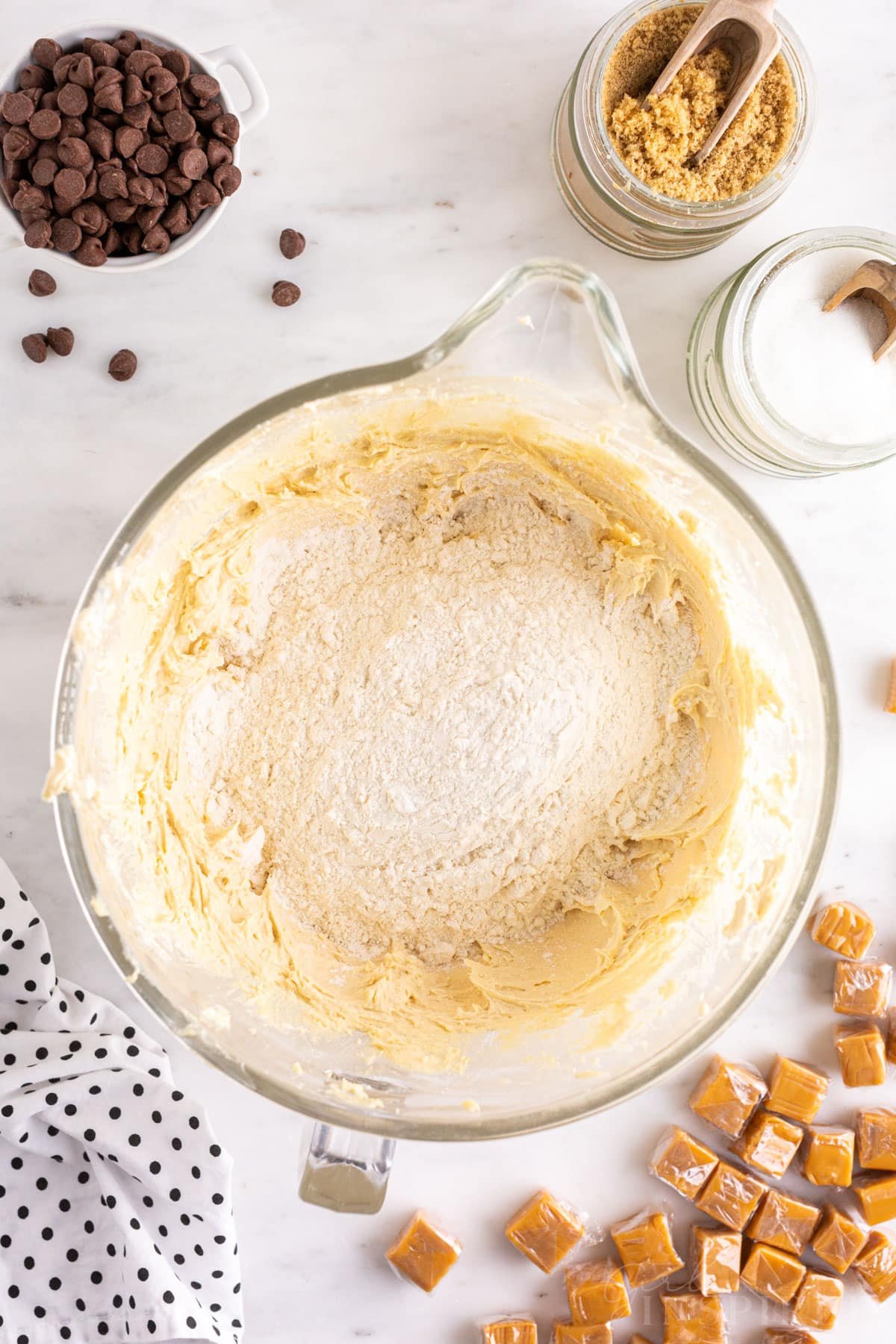 Mixing bowl with wet and dry cookie dough ingredients, salted caramel cookie bar recipe ingredients on a countertop.