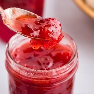 Spoonful of strawberry rhubarb jam lifted from jam jar.