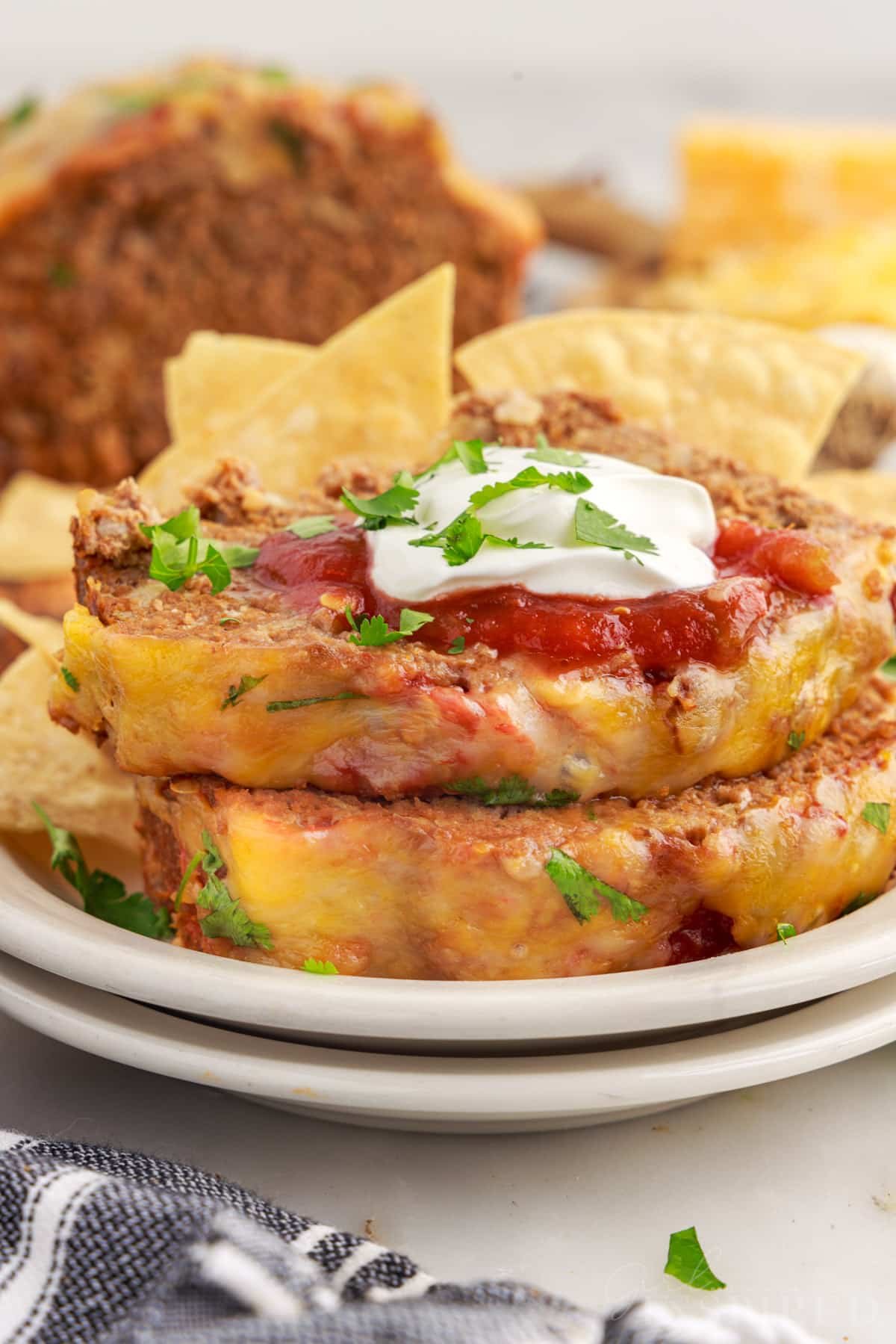 Two slices of Taco Meatloaf on two stacked plates with sour cream on top.