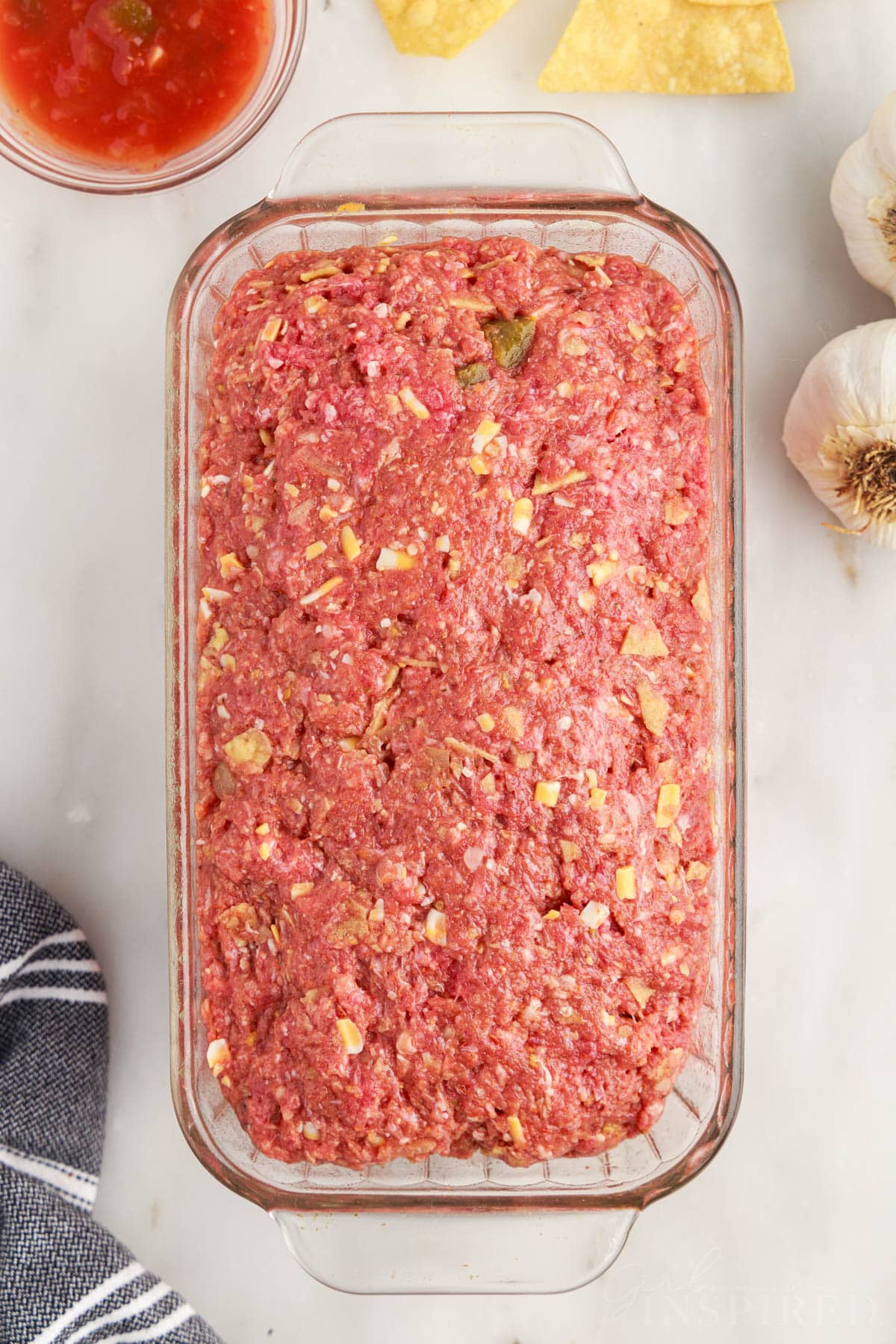 Meatloaf ingredients shaped into a loaf and placed into a glass loaf pan.