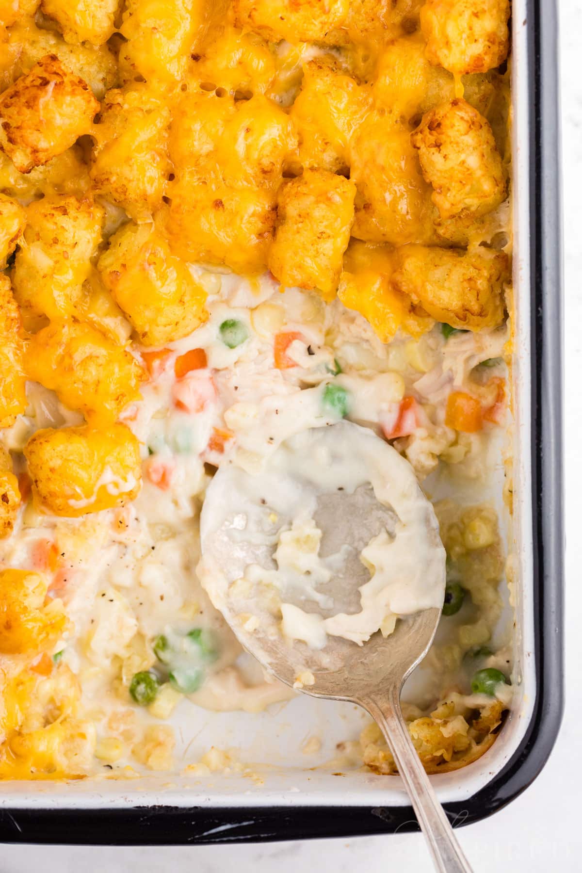 Overhead view of tater tot chicken pot pie in a casserole dish with a spoon resting in scooped out corner.
