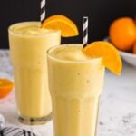 Two glasses of Orange Julius recipe with orange wedge garnish and decorative straws.