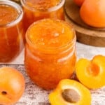 Close up of Apricot Pineapple Jam in glass jars, fresh apricots on a wooden countertop.