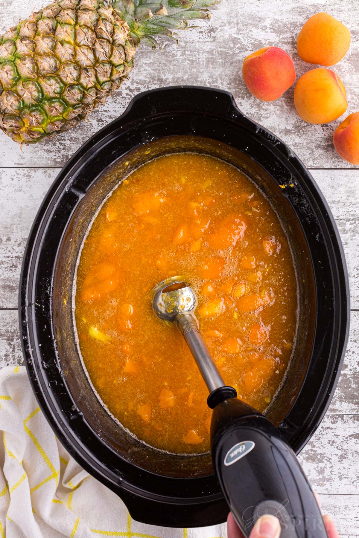 Apricot pineapple jam mixture blended by an immersion blender in a Crockpot.