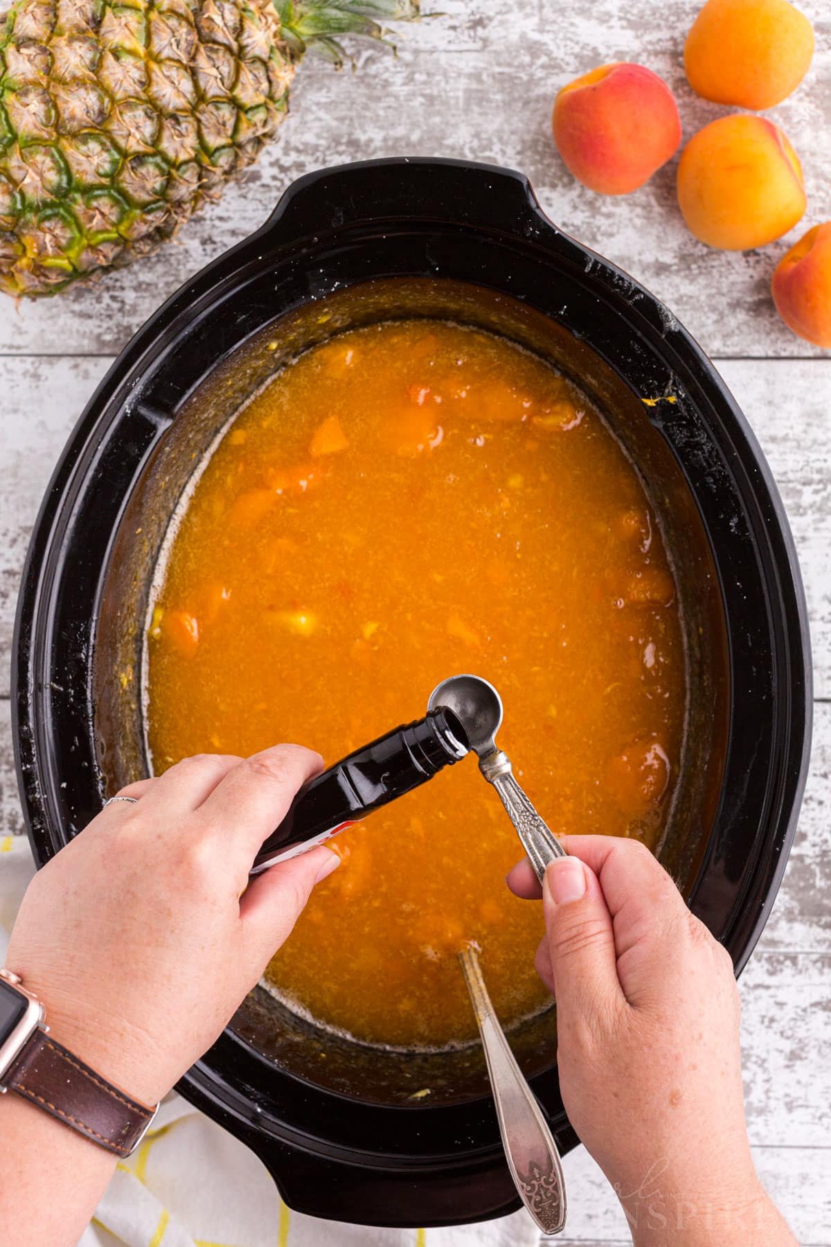 Almond extract added to cooked apricot pineapple jam mixture in a Crockpot.