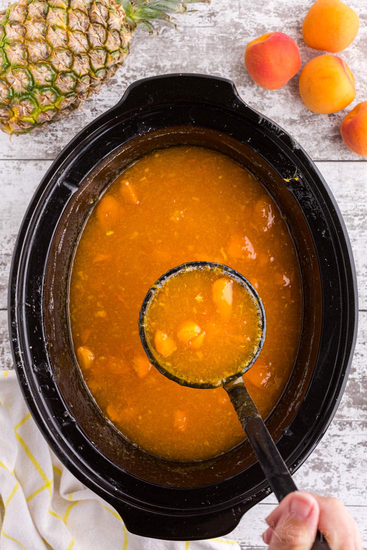 Ladle filled with apricot pineapple jam held above Crockpot filled with jam mixture.