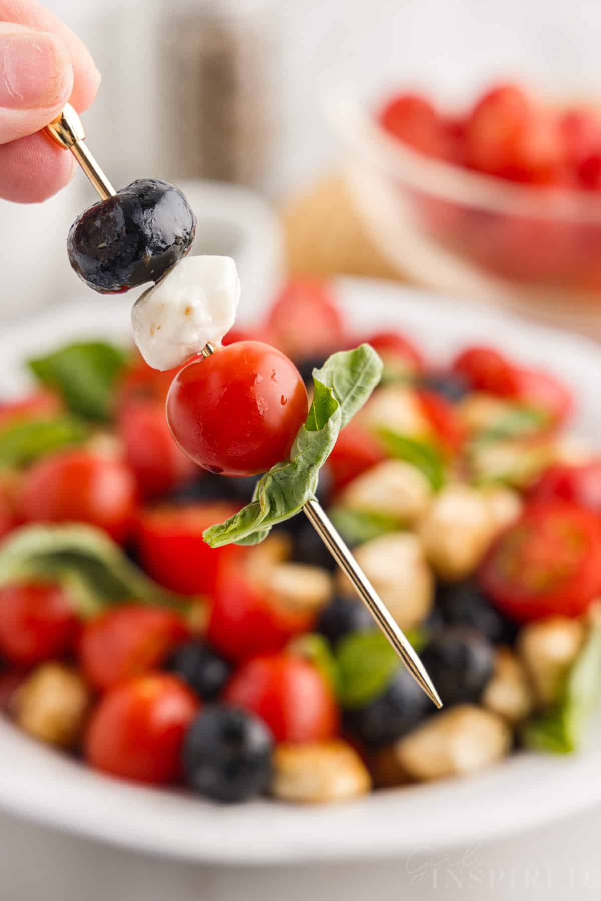 A skewer with a blueberry, piece of mozzarella, a tomato and a piece of basil.