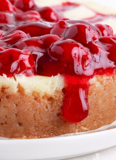 Cherry cheesecake on white platter with cherries spilling over the edge.
