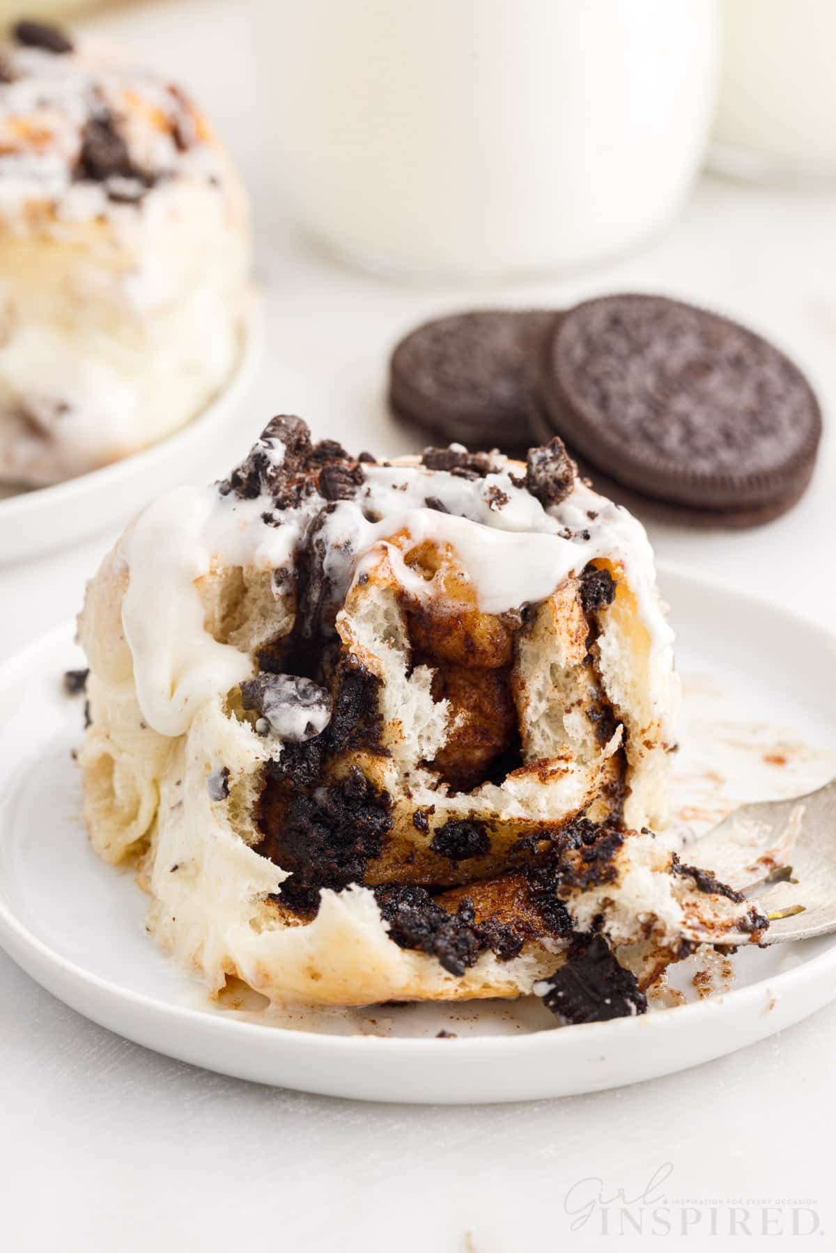 A Cookies and Cream Cinnamon Roll on a plate with a bite taken from the front.