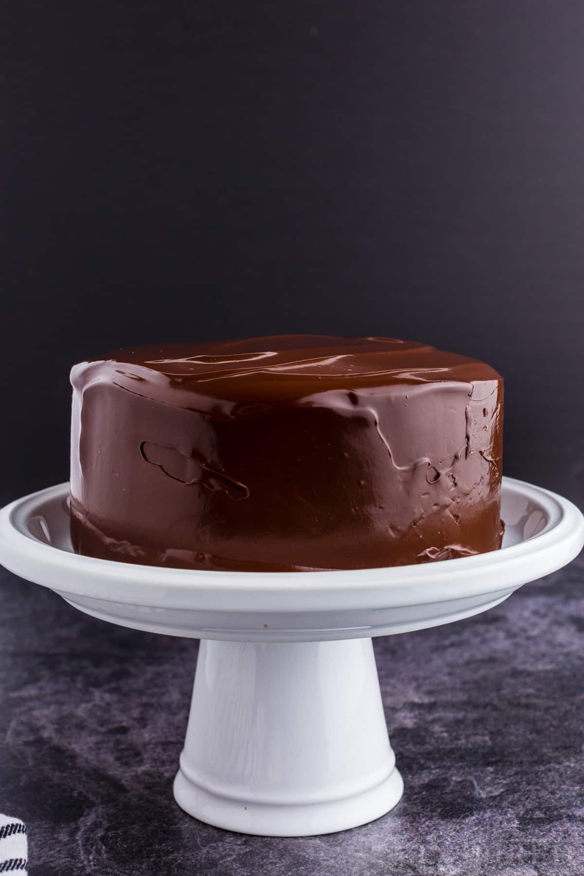 A cake on a stand covered in Dark Chocolate Ganache.