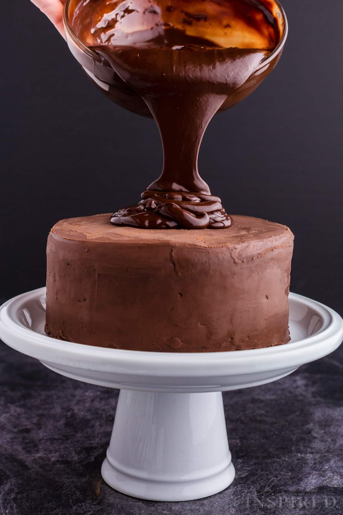 A cake on a tiered tray, Dark Chocolate Ganache poured on top.