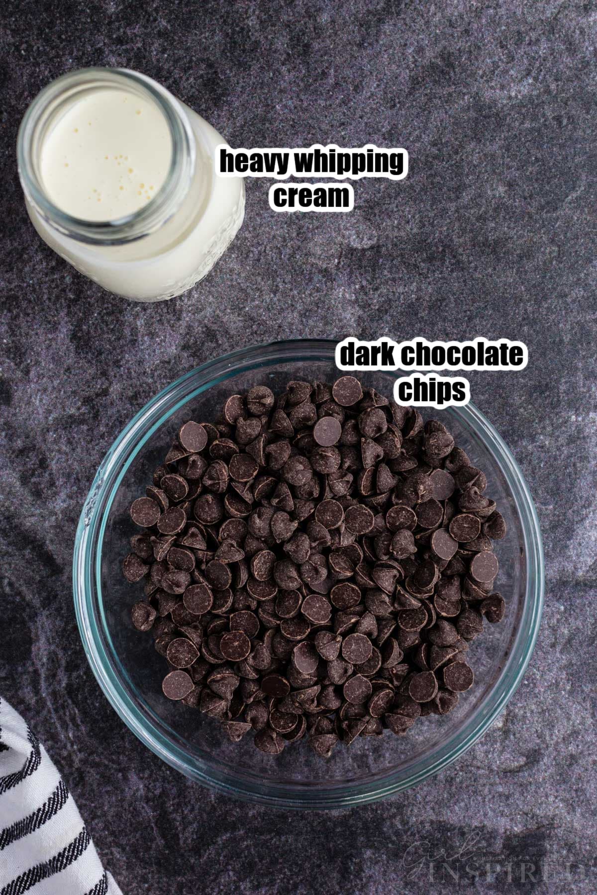 Dark chocolate chips in a bowl next to a cup of heavy whipping cream.