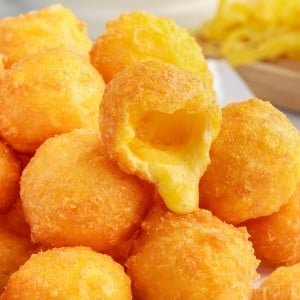 Front close up of a pile of Fried Cheese Balls, one with a bite taken from it.