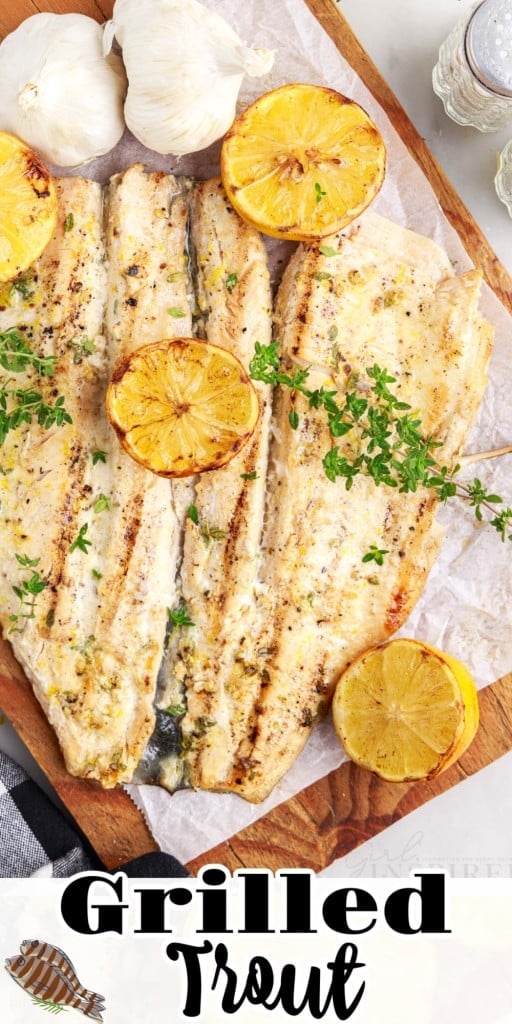 Grilled Trout on a wooden board, served over a parchment paper with half-cut lemons, scattered herbs and two whole garlics placed around