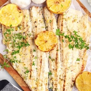 Grilled Trout on a cutting board with fresh herb sprigs and grilled lemon halves.