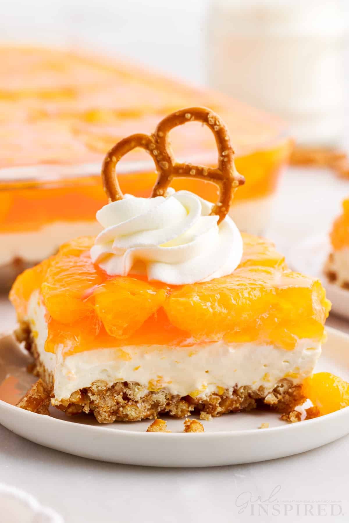 Orange Pretzel Salad on a small dish with whipped topping and a pretzel on top.