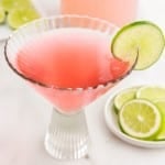 Decorative glass with Pink Flamingo Drink garnished with a lime next to a dish of limes.