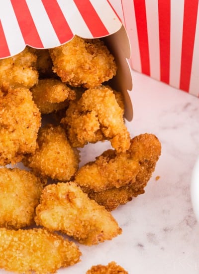 Popcorn chicken in decorative paper boxes, bowl of dipping sauce on the side on a white marble counter top