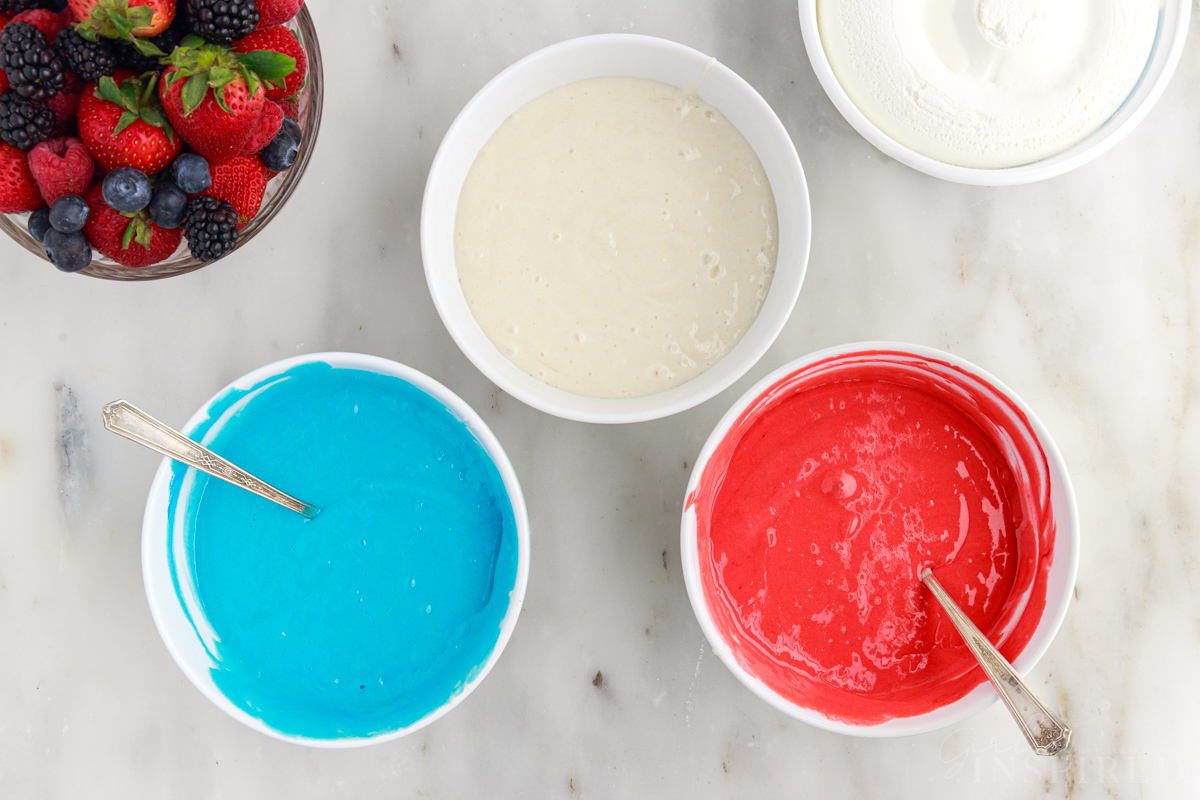 Red, white, and blue cake batter in mixing bowls.