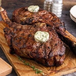 Two cooked Tomahawk steaks on a wooden kitchen board.