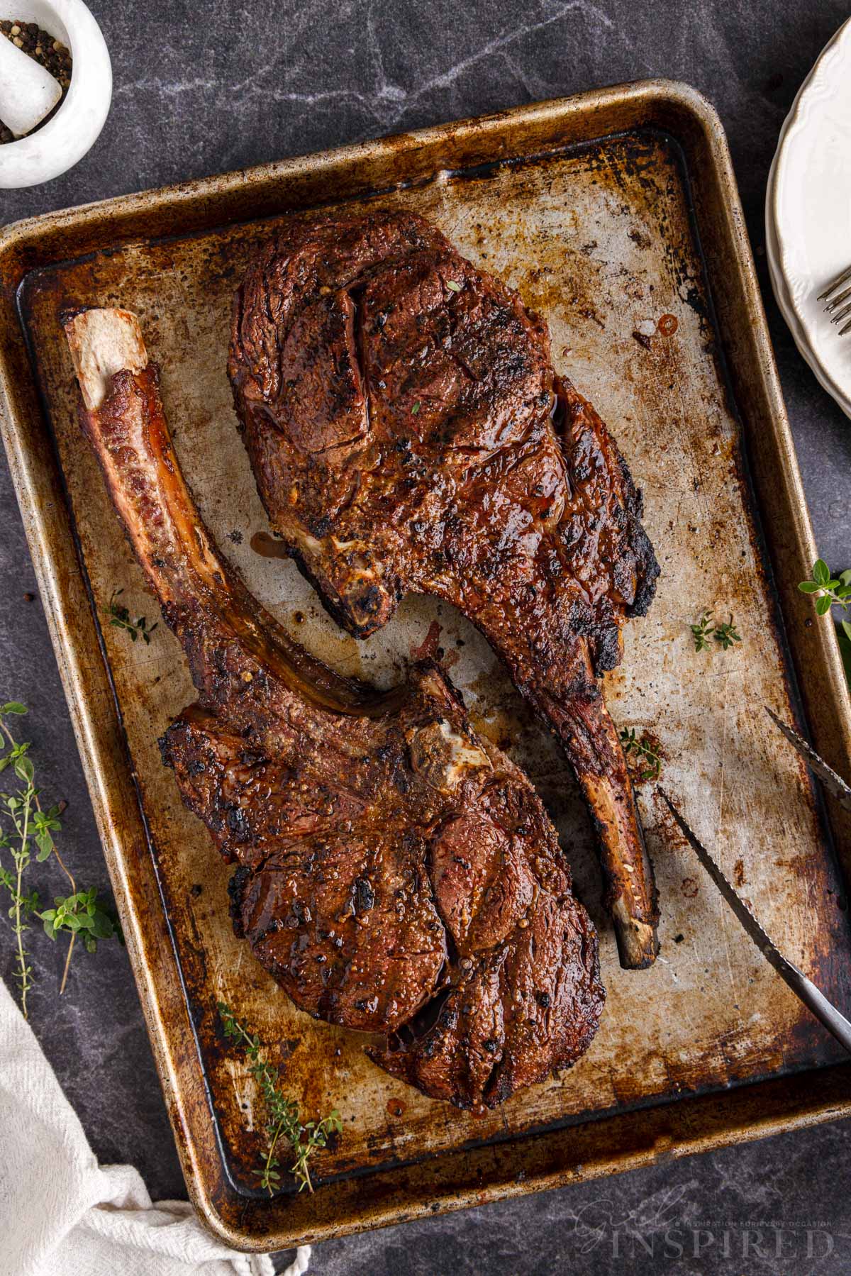 Two Tomahawk steaks on a metal baking sheet.