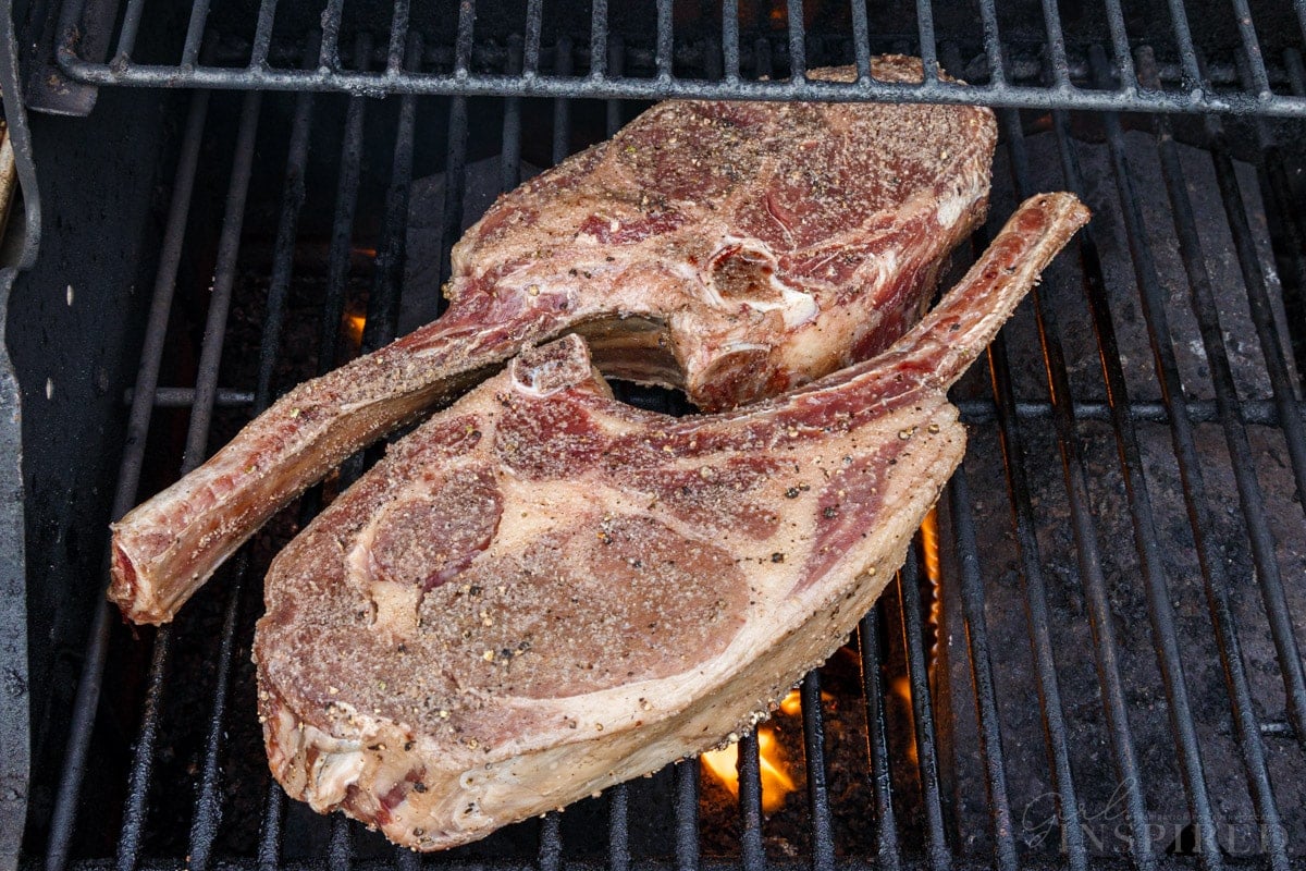 Two seasoned Tomahawk steaks on an oiled hot grill.