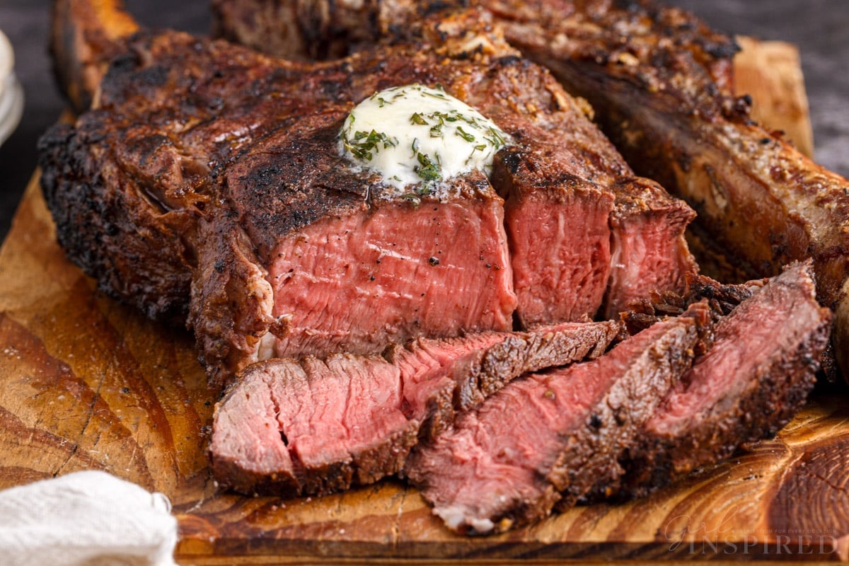 Sliced Tomahawk steak with compound butter on a wooden board.