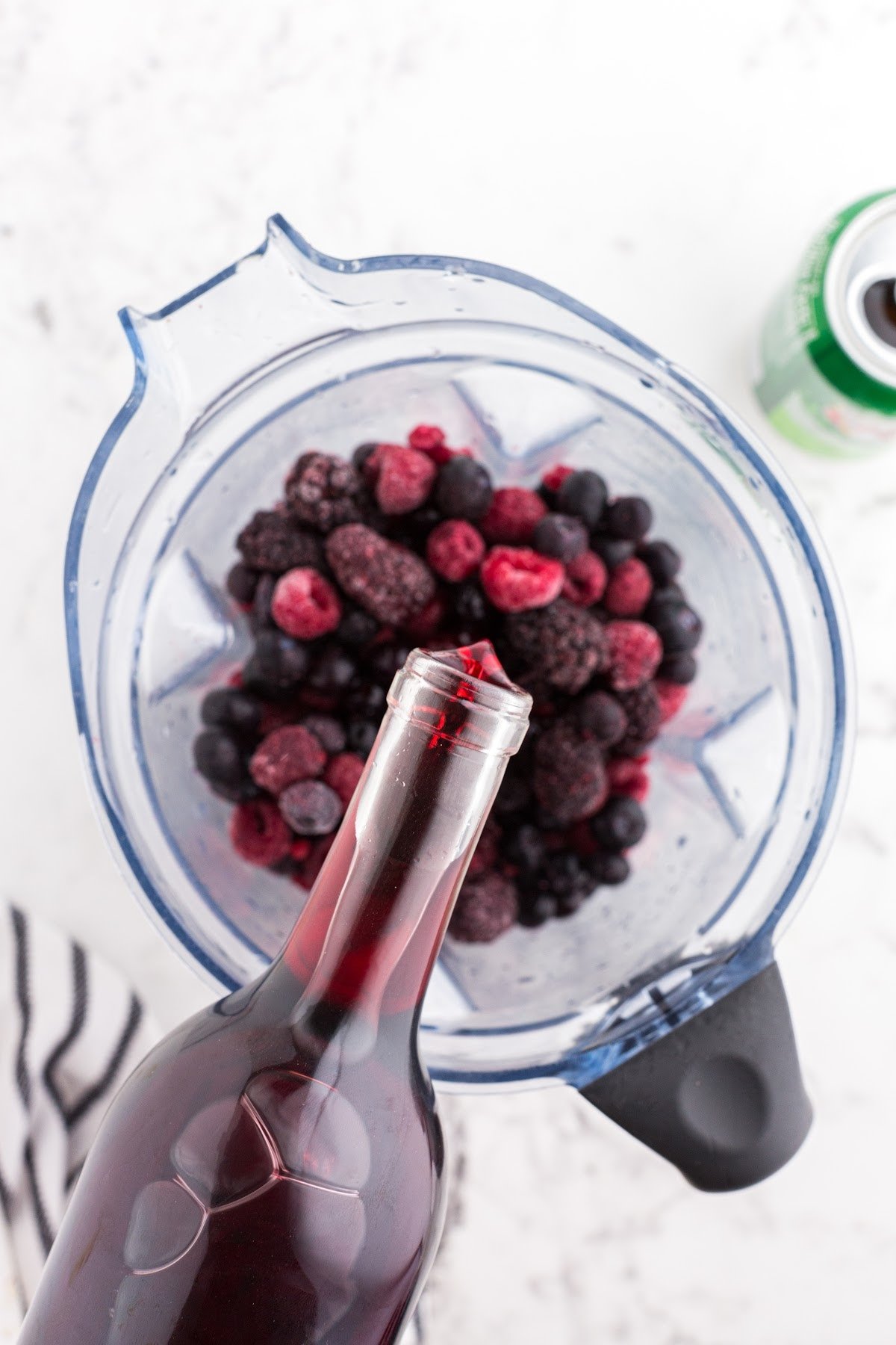 Red wine being poured over frozen fruit in a blender.