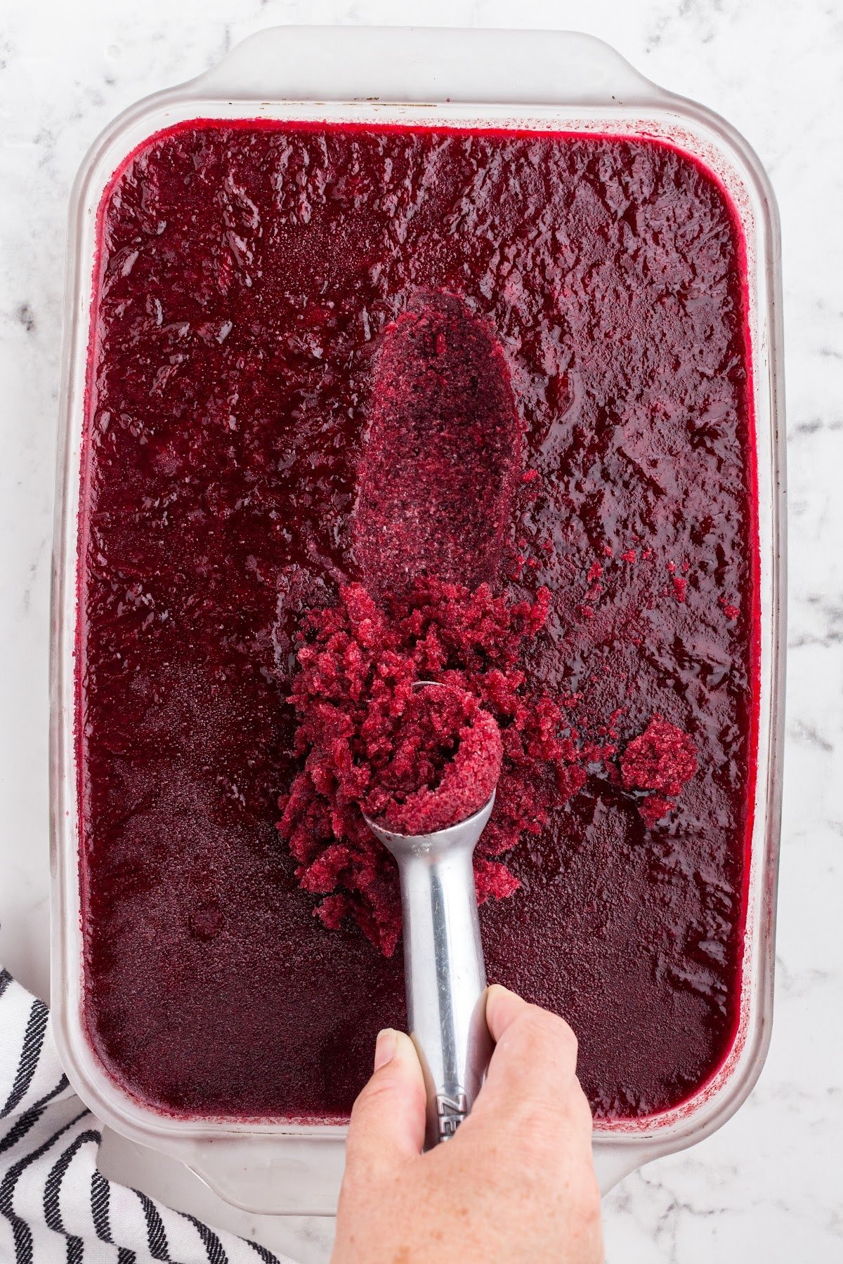 An ice cream scoop scooping out the frozen berry mixture from a 9x13.