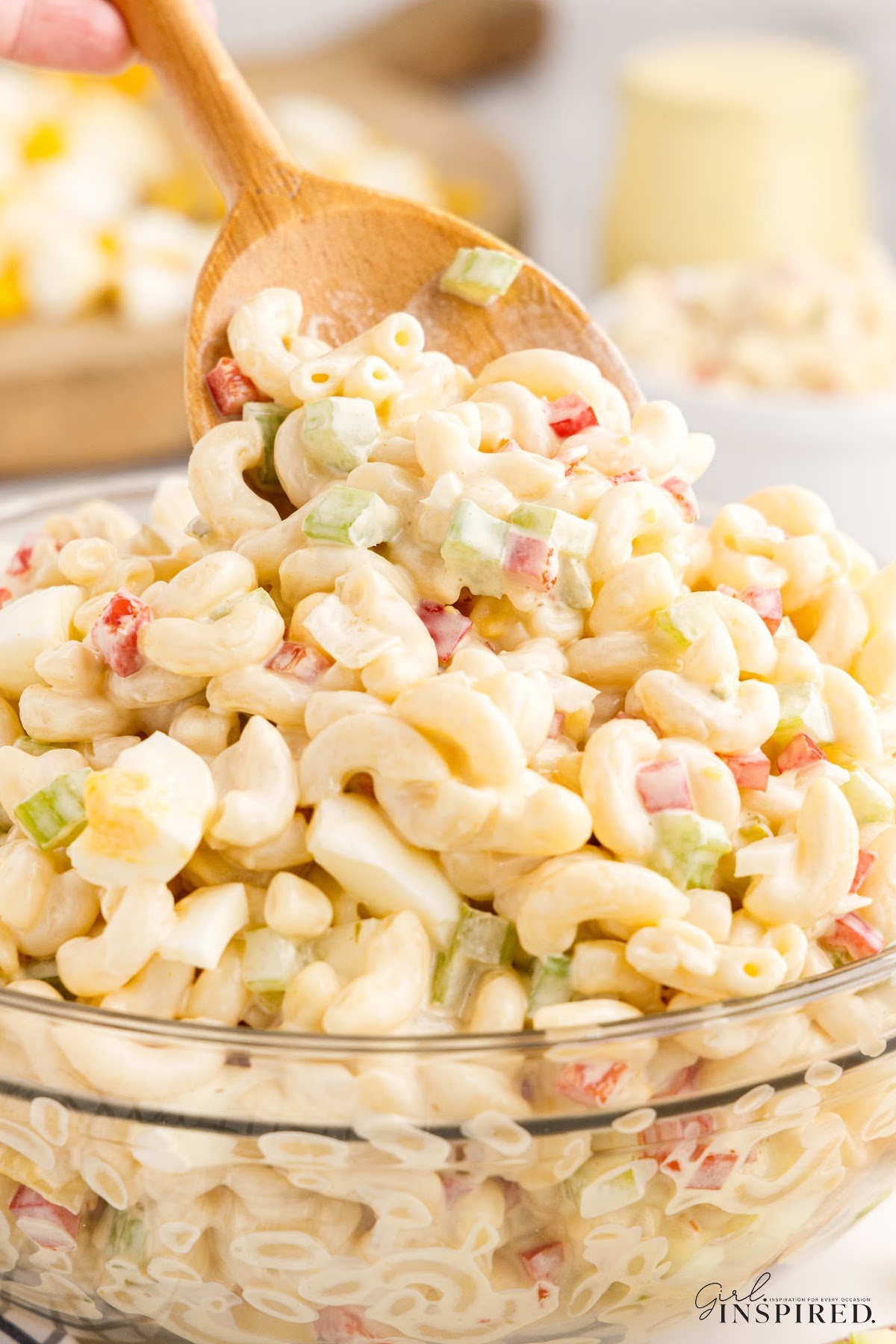 A dish of Amish Macaroni Salad with a wooden spoon scooping up some.