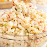 Front close up of Amish Macaroni Salad in a glass dish with a wooden spoon inserted.