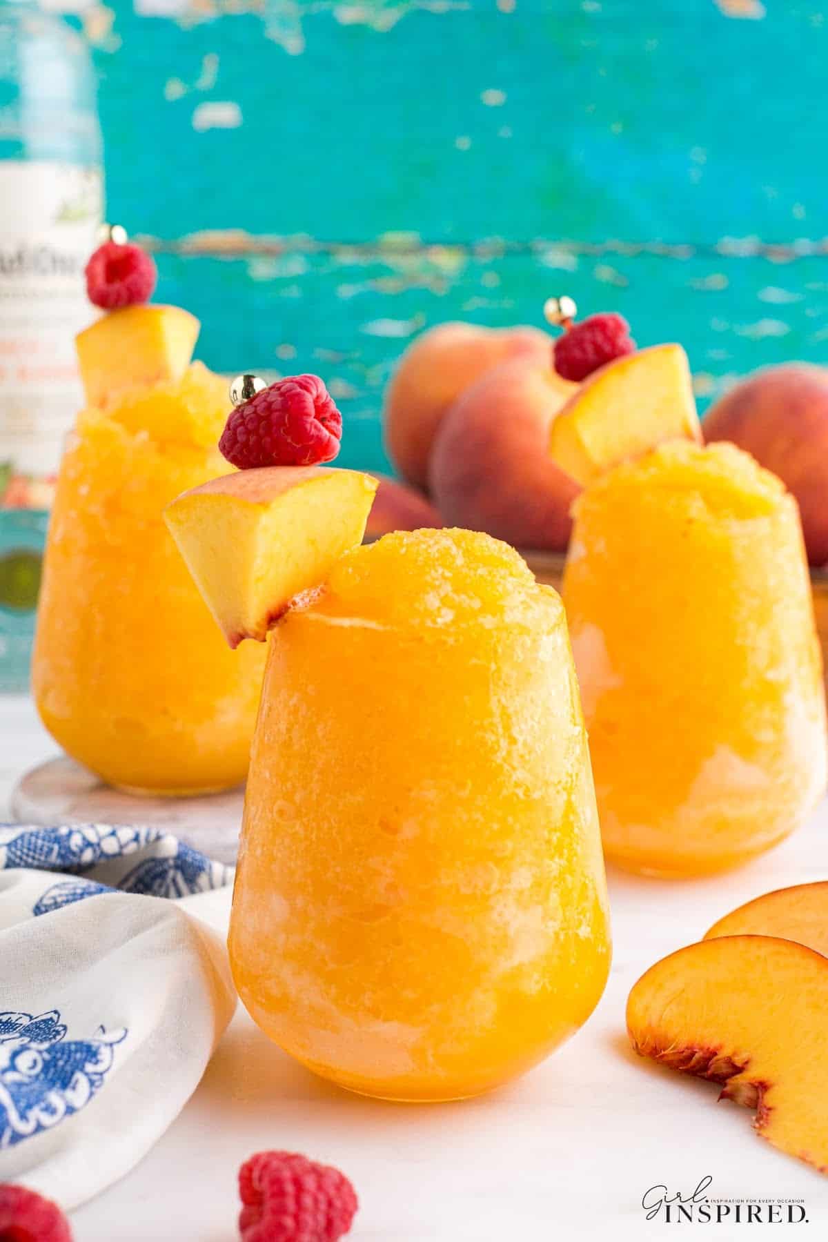 Three glasses of Peach White Wine Slushie garnished with peaches and raspberries.