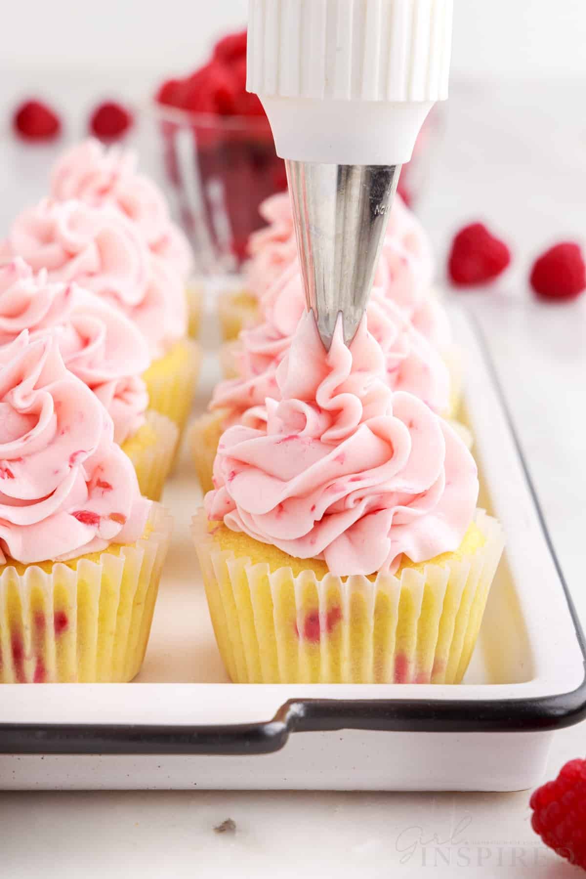 Piping tip applying a big swirl of raspberry frosting on top of the raspberry cupcakes.