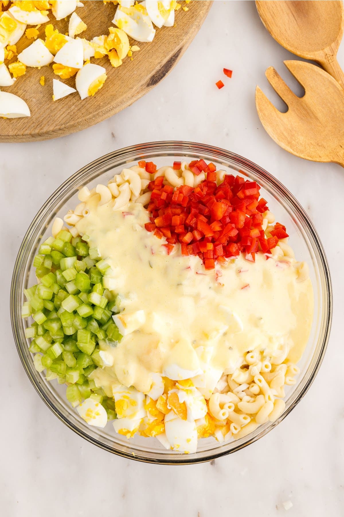 A mixing bowl of eggs, macaroni, peppers, celery, and mayo.