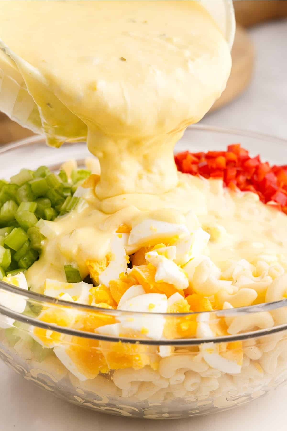 Amish Macaroni Salad dressing poured over ingredients in a mixing bowl.