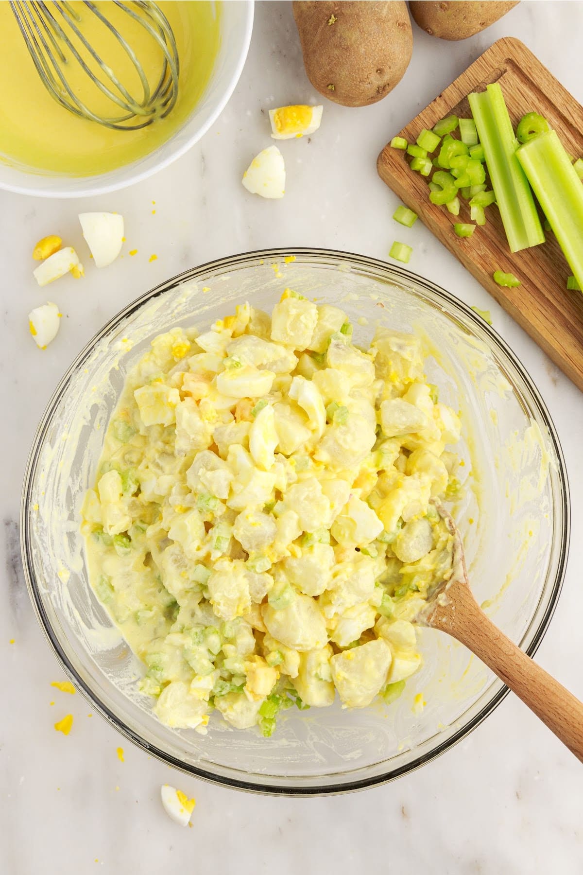 Amish Potato Salad stirred together in a mixing bowl with a wooden spoon.