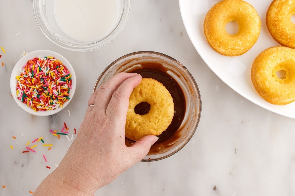 A Cake Mix Donut being dipped into chocolate.