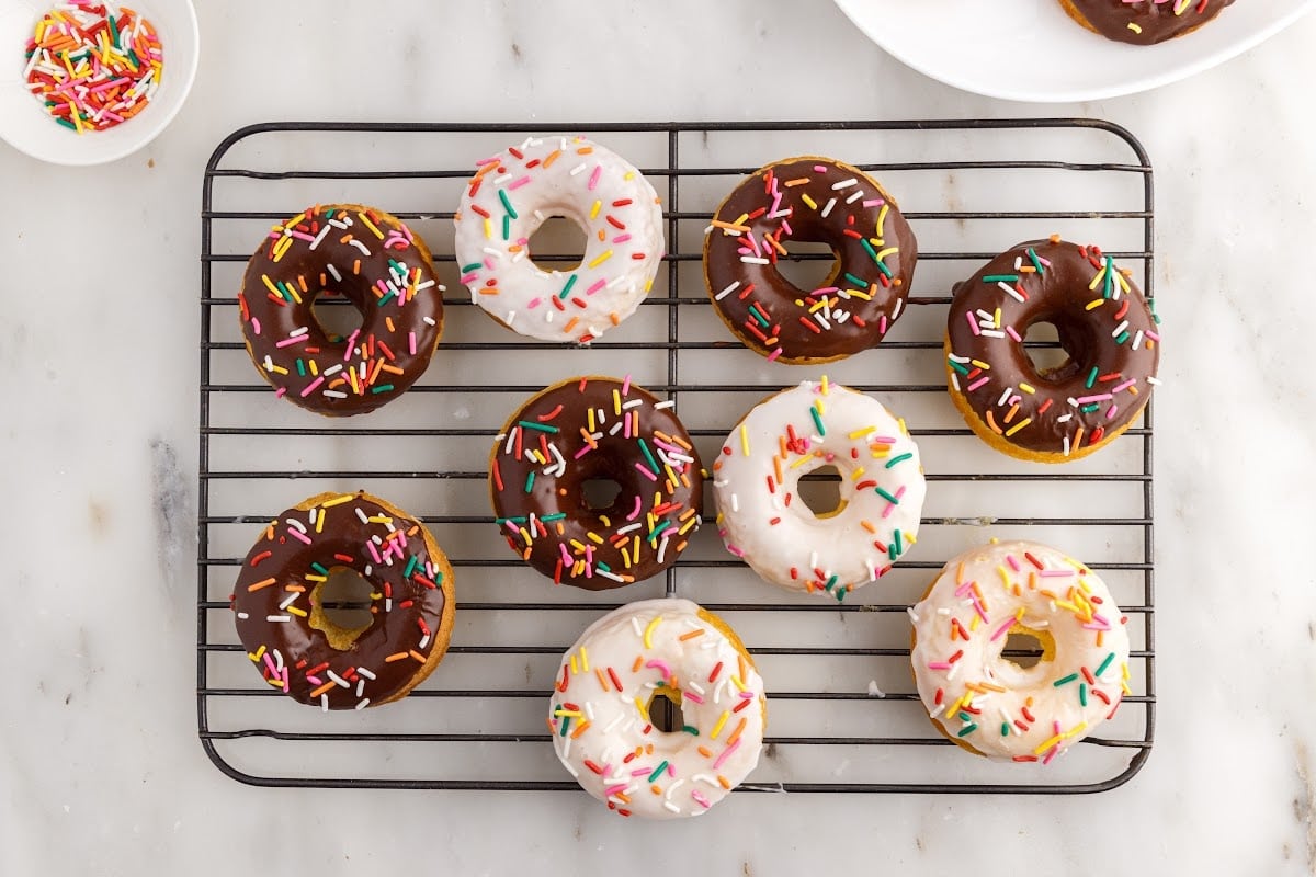 Cake Mix Donuts on a cooling rack iced with white and chocolate icing with sprinkles.