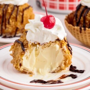 Deep fried ice cream with a bite taken out on a plate topped with whipped cream and a cherry.