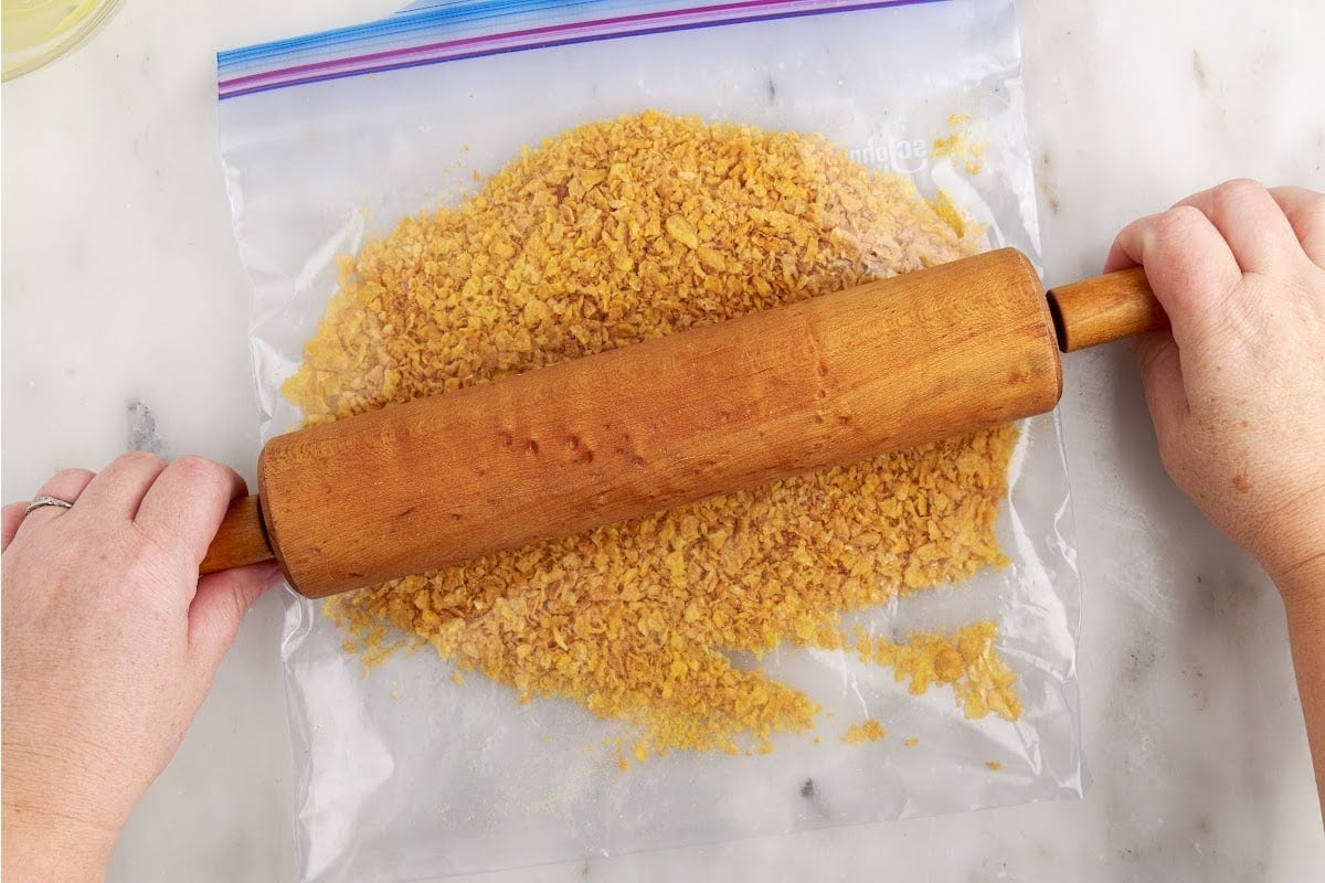 Crushing the corn flakes in a plastic bag using a rolling pin.