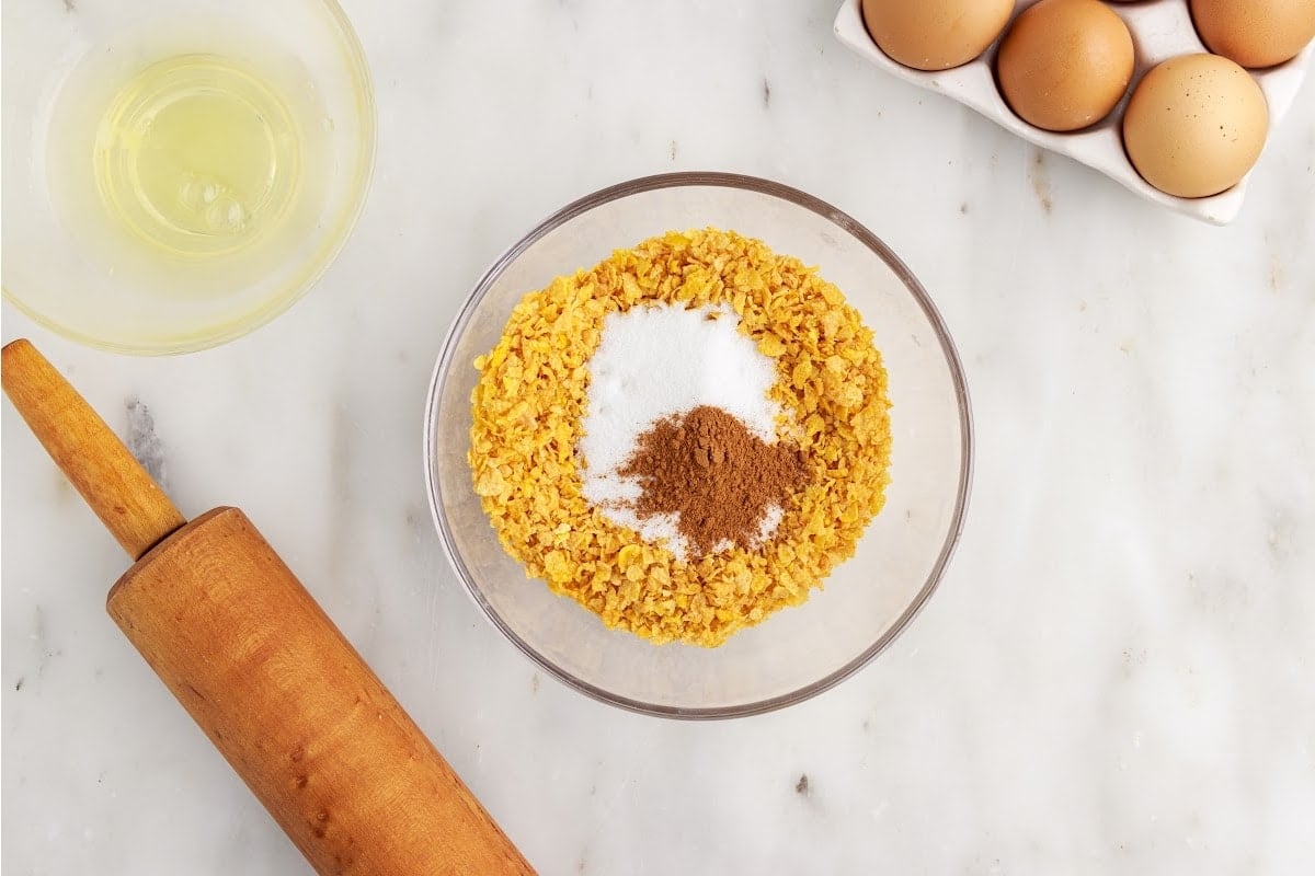 Corn flakes, sugar, and cinnamon in a glass mixing bowl.