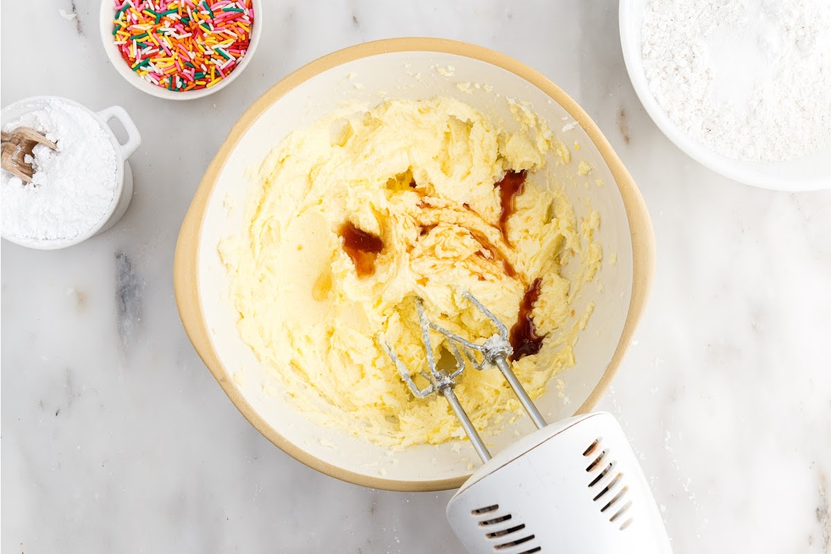 Vanilla added to egg mixture in a mixing bowl mixed with a mixer.