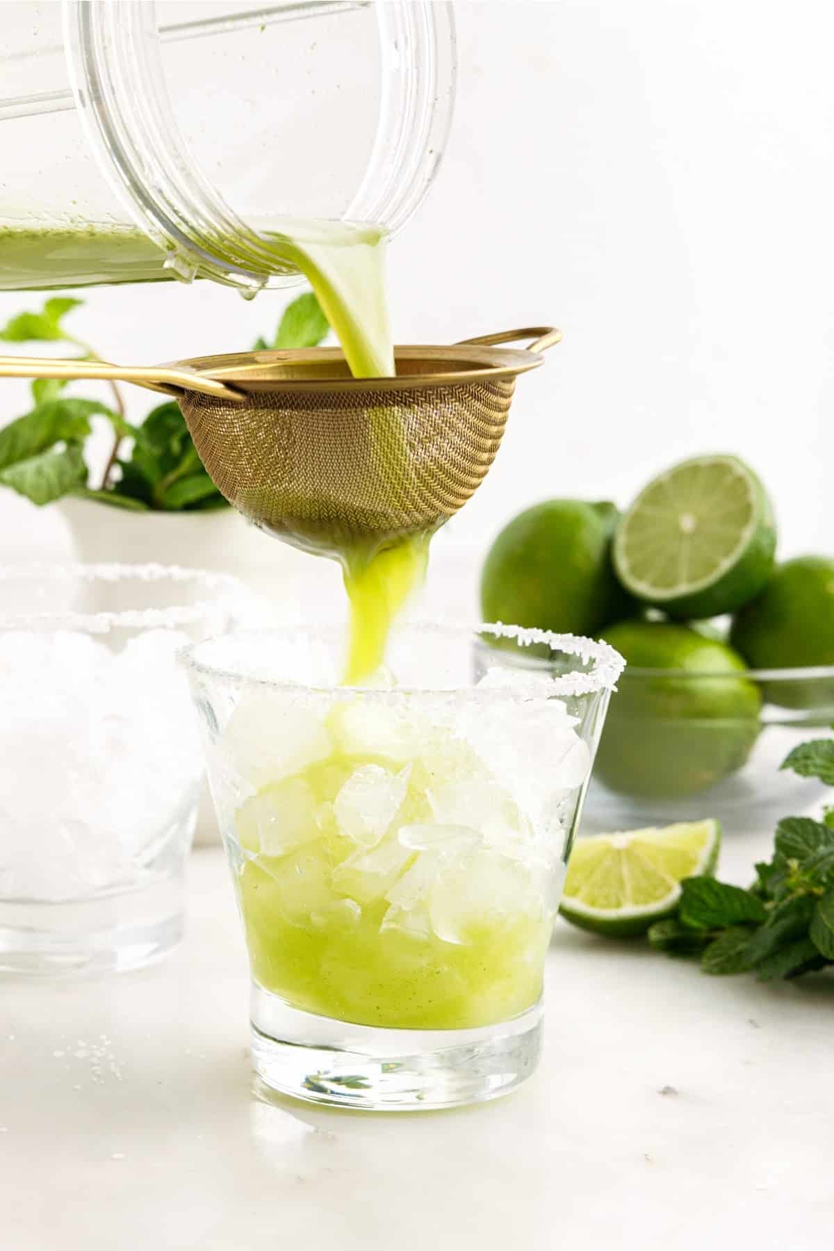 Mint mixture poured over a small strainer into a glass with ice.